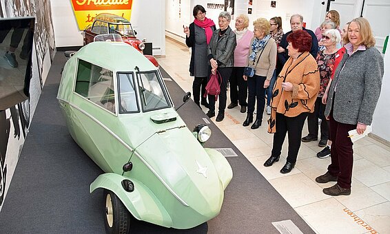 Seniorinnen und Senioren des BRK Heims Rosenheim erkunden zusammen mit der Historikerin Lydia Zellner (im Bild links) eine Ausstellung in der Rosenheimer Galerie zum Thema 100 Jahre Design in Rosenheim. | © Stefan Trux Eine Gruppe von Seniorinnen und Senioren betrachtet in der Städtischen Galerie Rosenheim einen lindgrünen Oldtimer