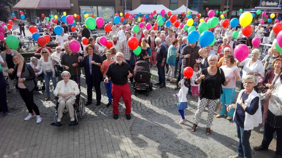 Auf diesem Foto sehen Sie einen Platz, auf dem sich viele Menschen unterschiedlichen Alters befinden