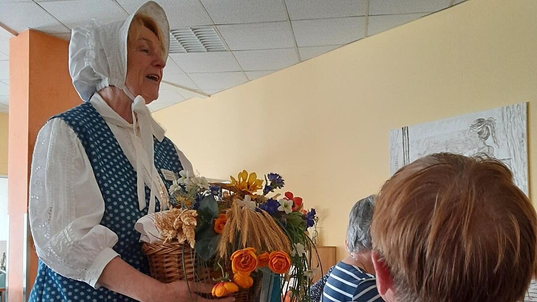 Eine Frau, verkleidet als Magd, hält einen Korb Blumen in der Hand