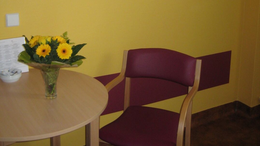 Foto: Blick in ein gelb gestrichenes Patientenzimmer, das auch durch Bilder an der Wand Orientierung gibt 