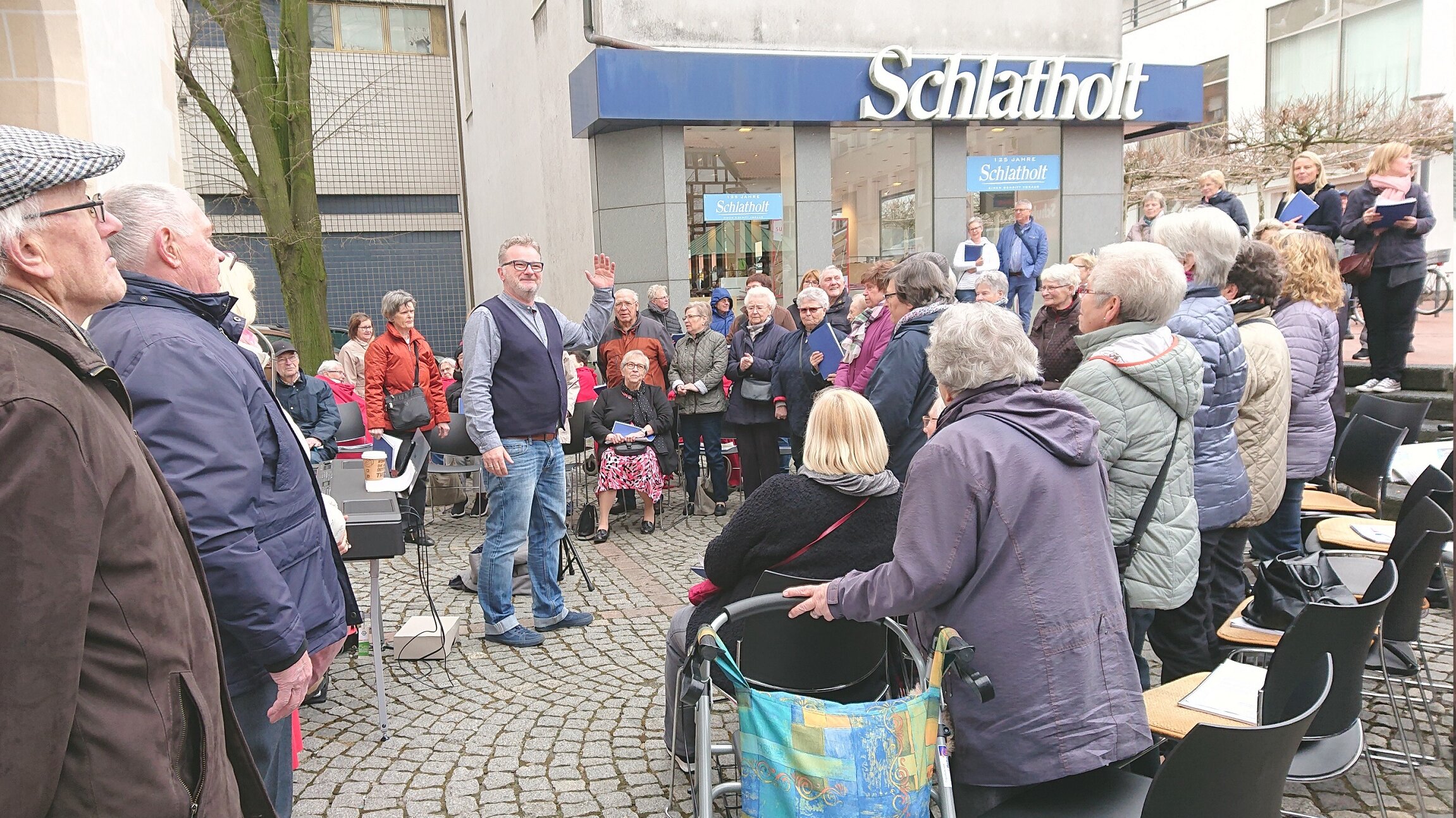 Auf diesem Foto sehen Sie einen öffentlichen Platz, auf dem viele ältere Menschen gemeinsam singen