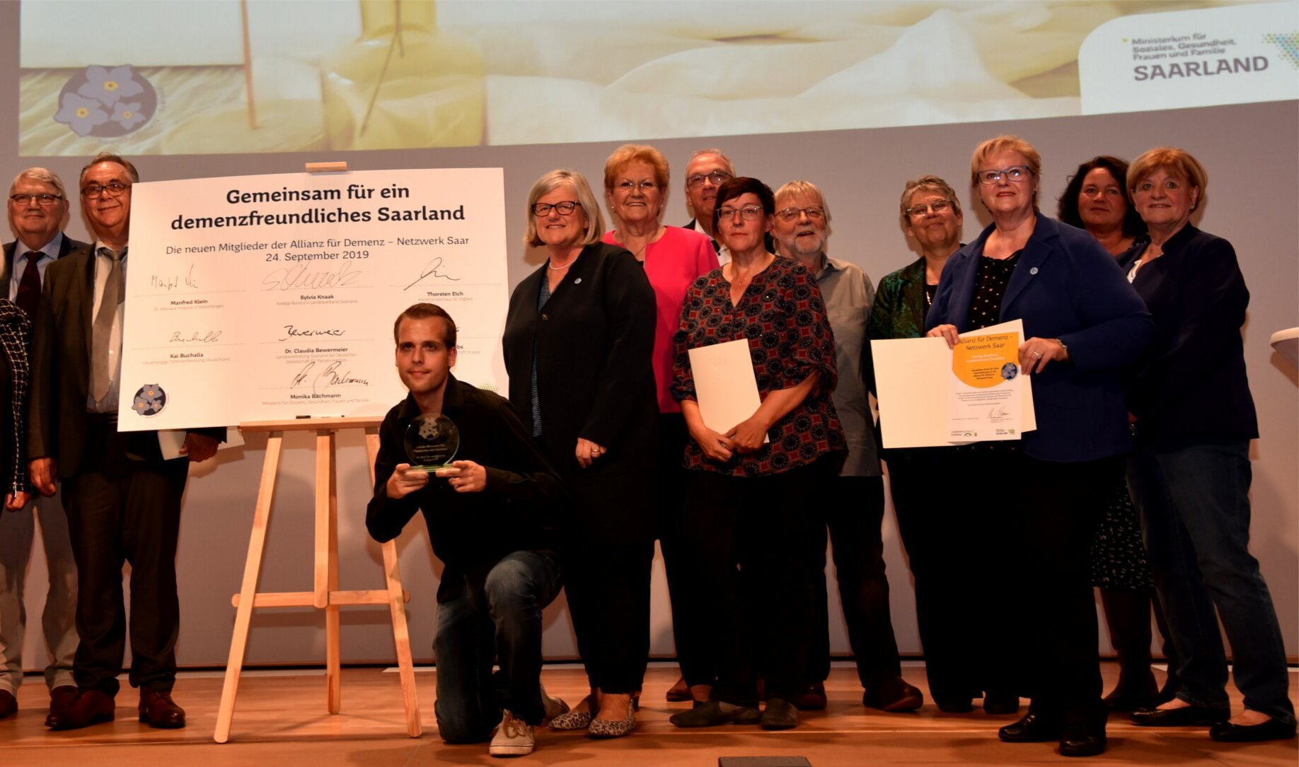 Die Projektbeteiligten des Vereins zur Förderung der Dorfentwicklung Hoof e.V. präsentieren auf einer Bühne ihre Auszeichnung