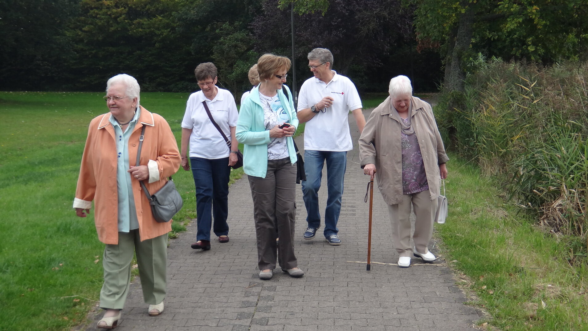 Die Dorfschwester Annetraud Kling geht mit einer Gruppe älterer Menschen im Park spazieren