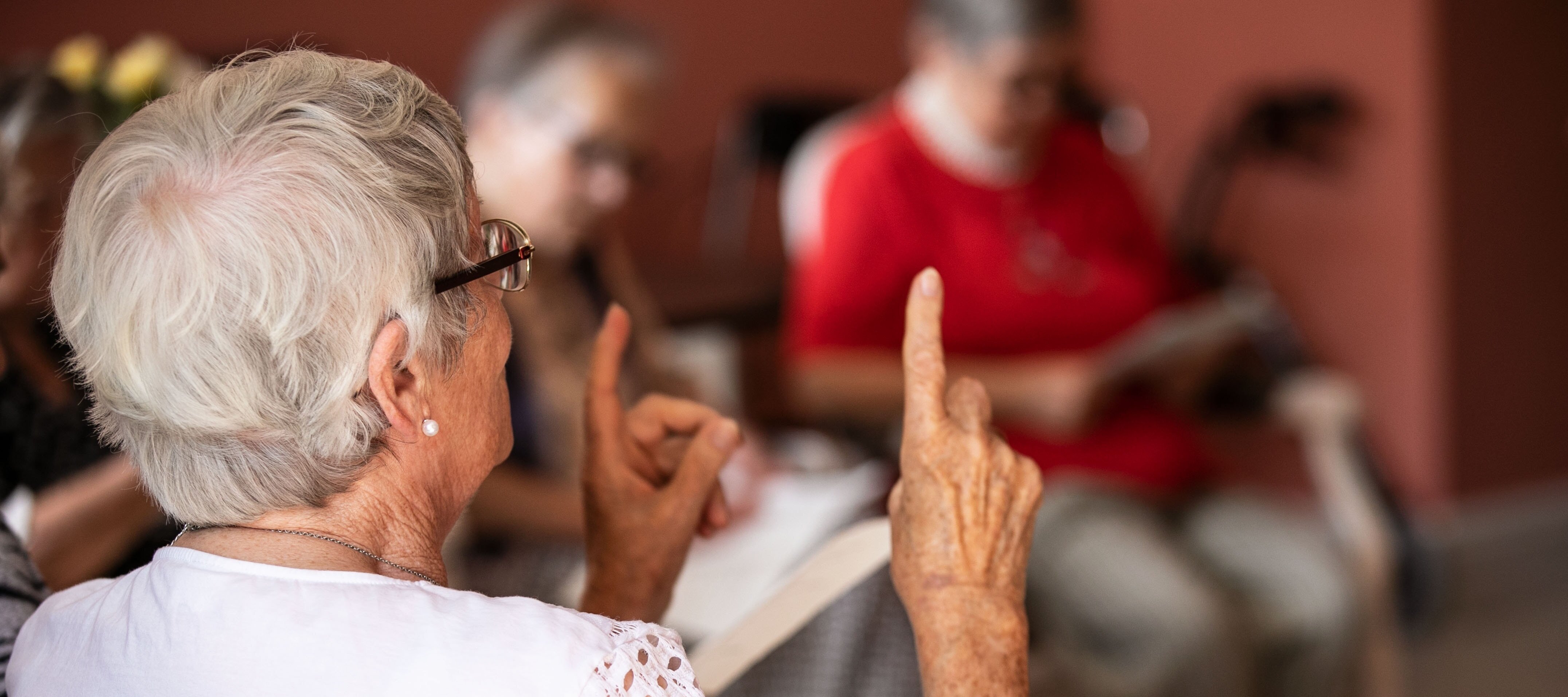 Foto: Ältere sitzende Frau von hinten, die ihre Zeigefinger in die Luft hält