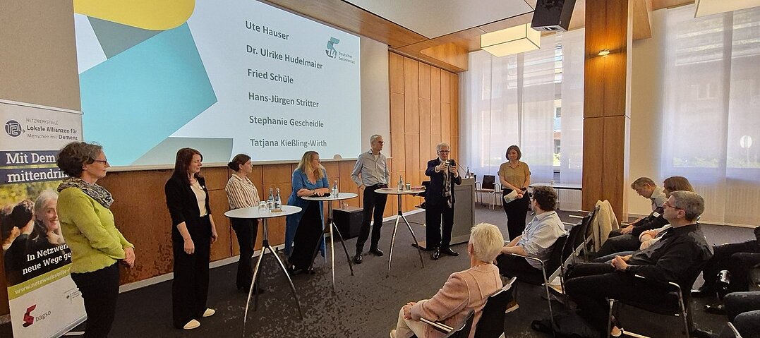 Die sechs Mitwirkenden sowie die Moderatorin stehen an Stehtischen