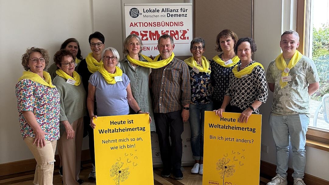 Foto: Seniorengruppe vor Stellwand halten zwei gelbe Schilder zum Weltalzheimertag vor sich