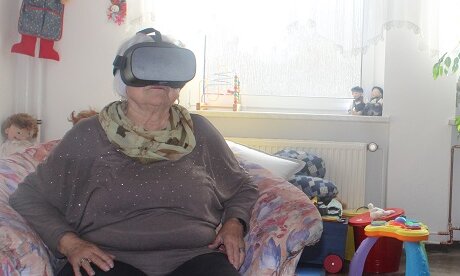 Eine ältere Frau und ein älterer Mann sitzen in einer Sitzgruppe und tragen Virtual-Reality-Brillen 