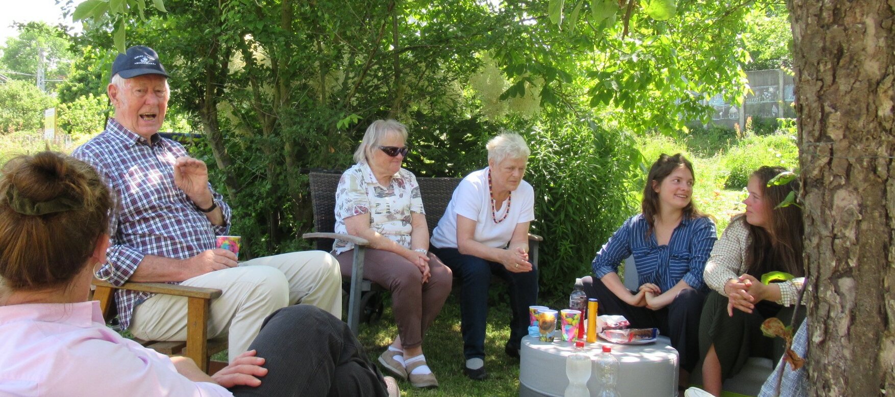 Sechs Gärtnerinnen und Gärtner sitzen in einem Halbkreis im Garten, unterhalten sich und genießen eine Trink- und Vesperpause.