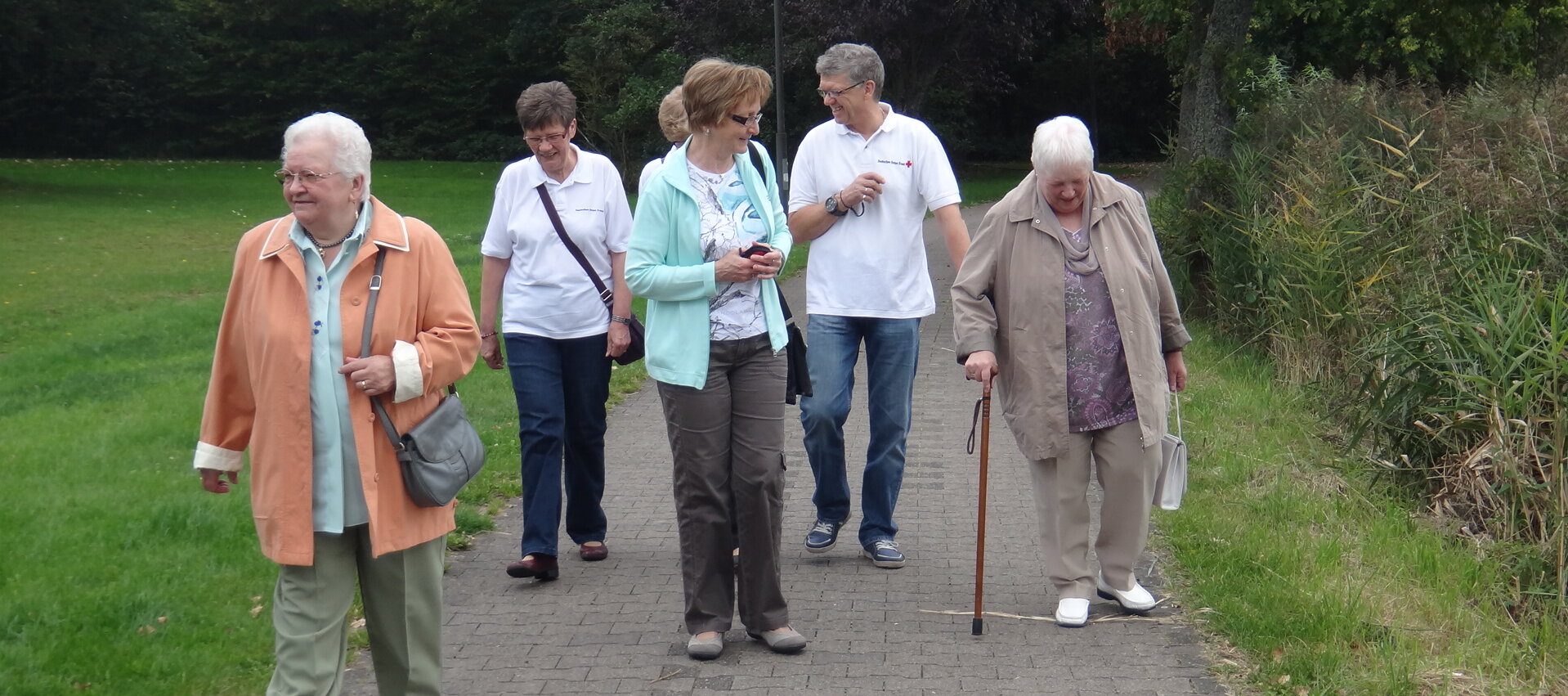 Foto: Die Dorfschwester Annetraud Kling geht mit einer Gruppe älterer Menschen im Park spazieren.