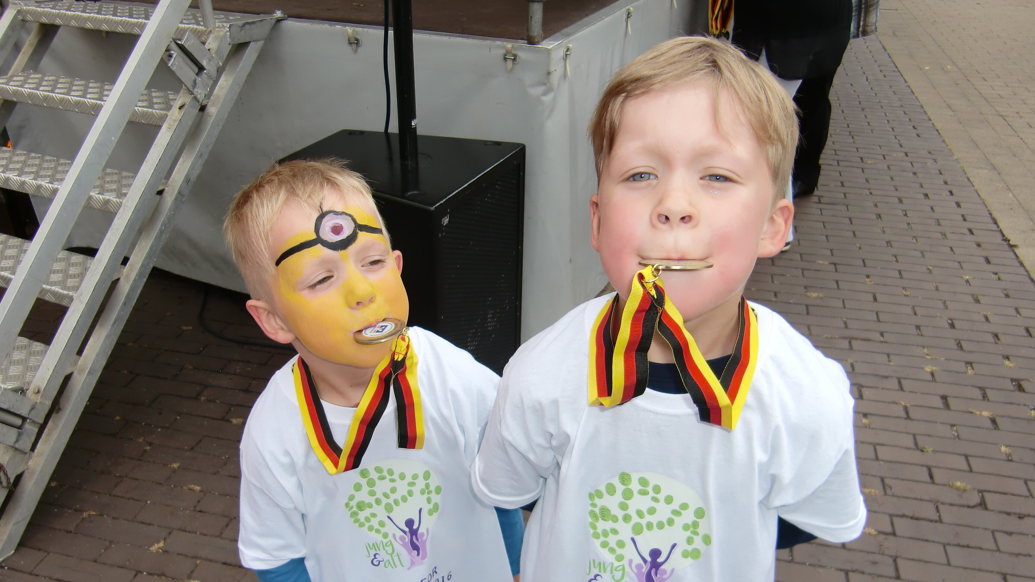 Auf diesem Foto stehen zwei kleine Jungs mit einer Medaille um den Hals