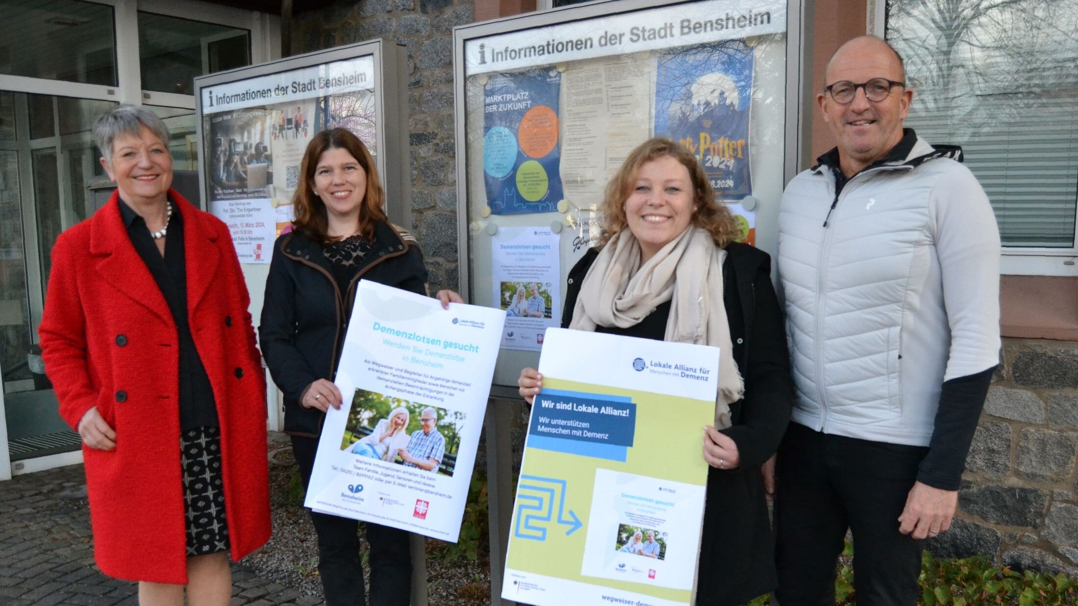 Foto: Vier Personen stehen vor einem Schaukasten der Stadt Bensheim. Zwei von ihnen halten jeweils ein Plakat in der Hand. 