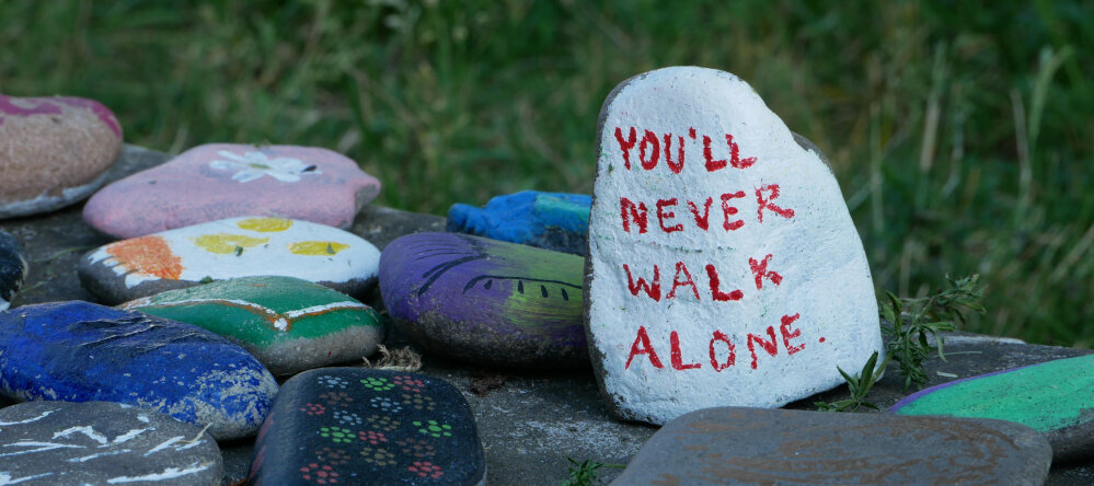 Bemalte Steine in der Landschaft. Auf einem Stein steht "You´ll never walk alone"
