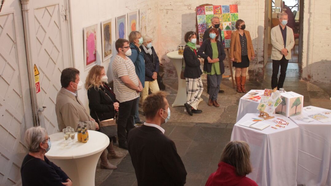 Innenraum einer Kirche, in der eine Gruppe von Menschen steht. An den Wänden hängen Kunstwerke