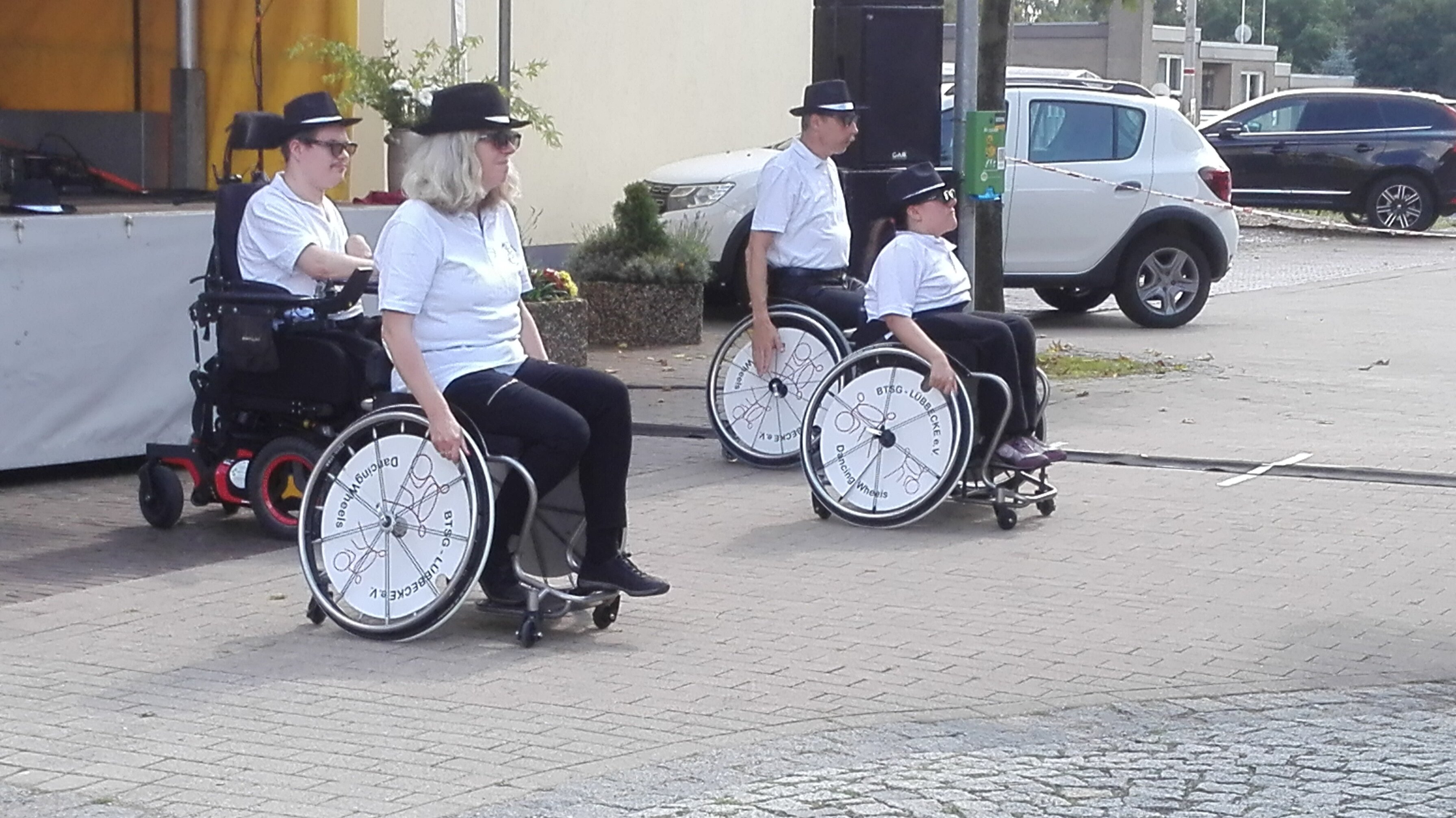 Auf diesem Foto sieht man vier Menschen unterschiedlichen Alters, die einen Tanz aufführen. Alle sitzen im Rollstuhl. 