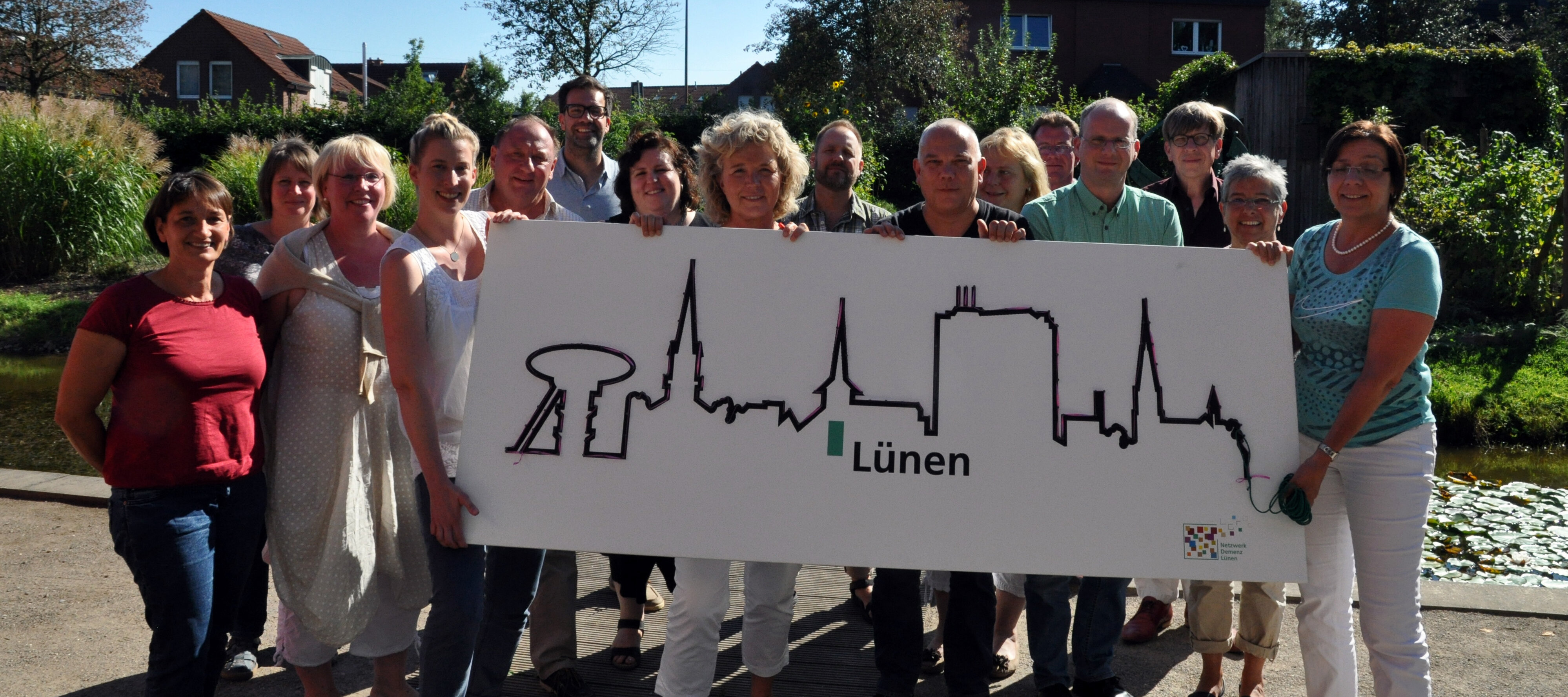 Eine Gruppe hält gemeinsam ein großes weißes Schild hoch. Darauf zu sehen die Umrandung der Dächer der Stadt Lünen.