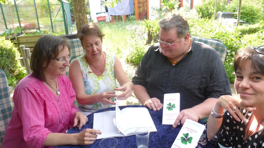 Foto: Vier Personen, die draußen an einem runden Tisch sitzen und an einem Flyer arbeiten.
