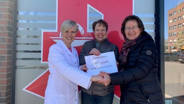 Foto: Drei Frauen, die vor einer Apotheke und mit einer Spende in der Hand fotografiert werden.