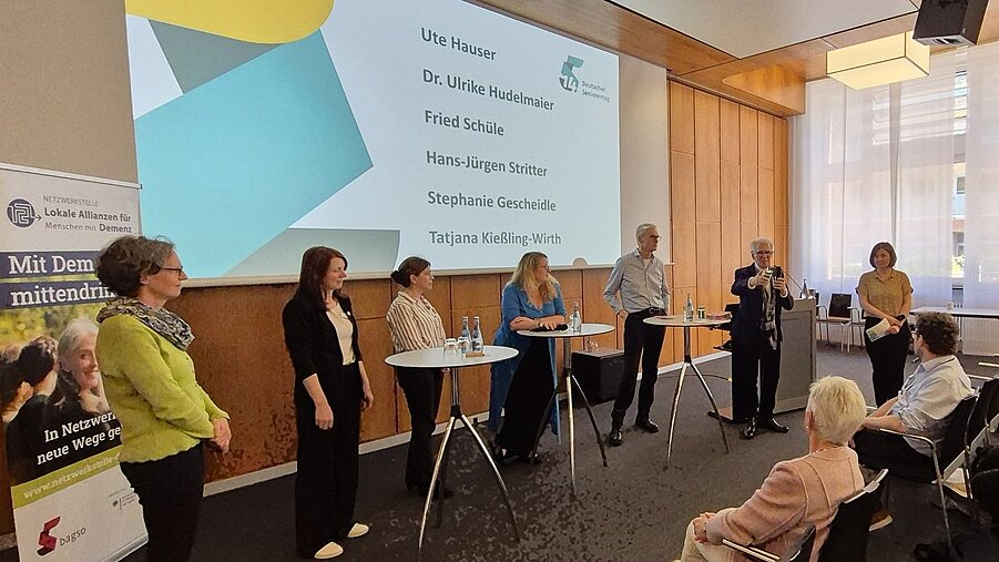 Die sechs Mitwirkenden sowie die Moderatorin stehen an Stehtischen