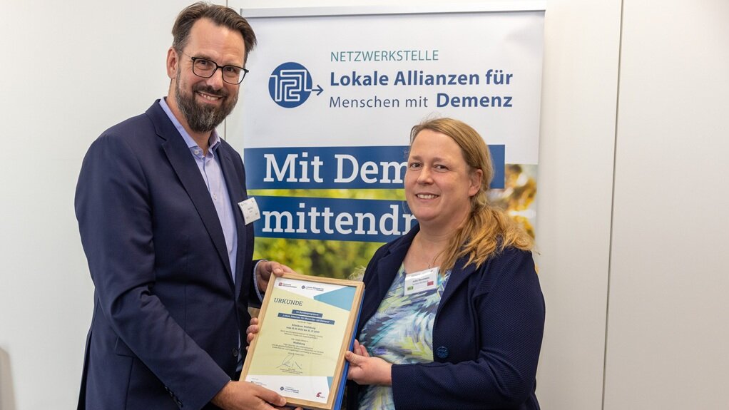 Urkundenverleihung durch Sven Paul, BMBFSFJ. Geehrt wird eine Lokale Allianz aus Niedersachsen (Klinikum Wolfsburg), vertreten durch Julia Neumann.  Foto: Herr Paul überreicht einer Frau eine Urkunde zur Würdigung ihrer Arbeit.