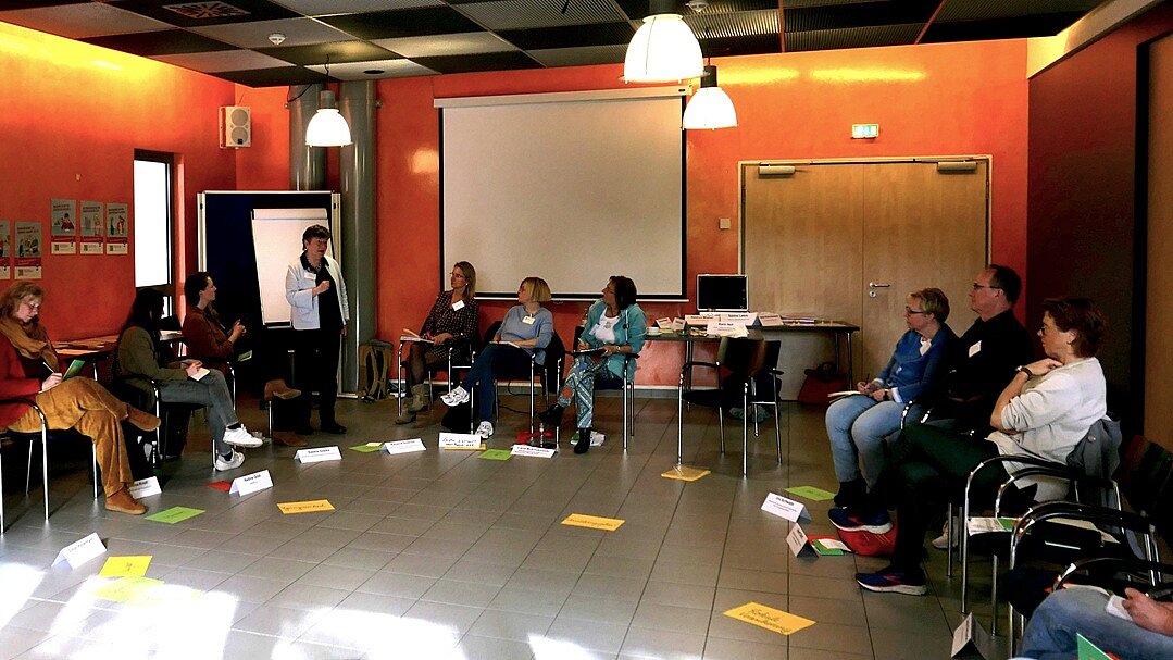 Die Teilnehmenden sitzen in einem Halbkreis, die Referentin steht und spricht zur Gruppe