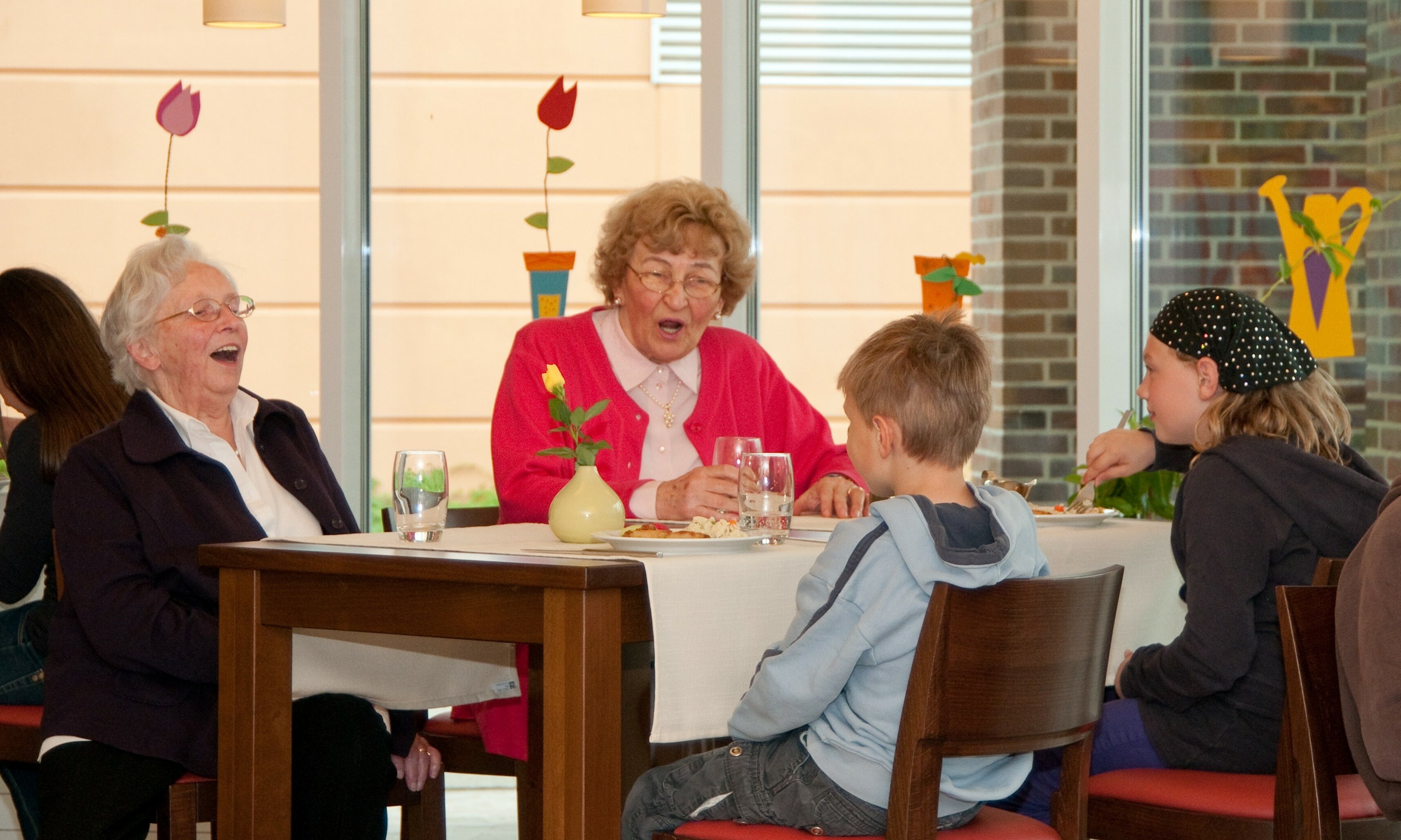 Zwei ältere Damen, die mit zwei Kindern an einem Tisch sitzen. 
