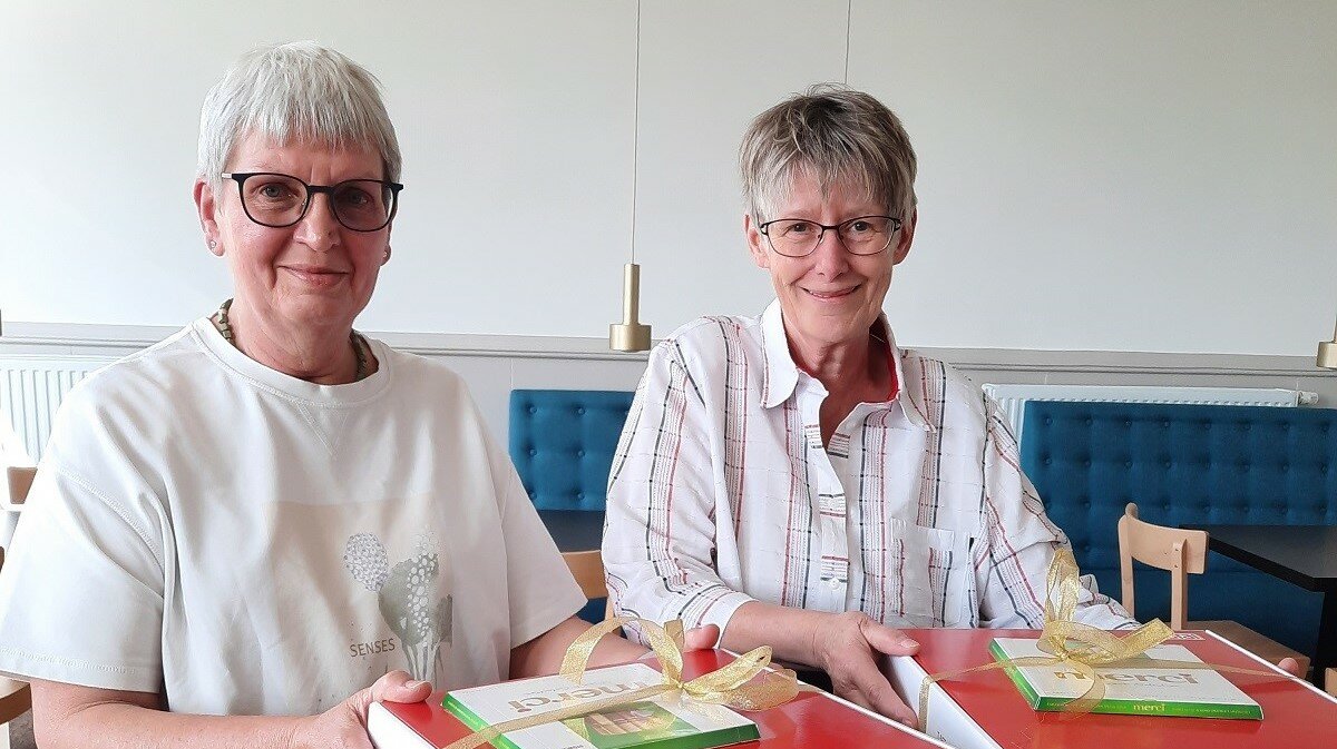 Zwei lächelnde Seniorinnen halten ein Geschenk mit Pralinen in der Hand.