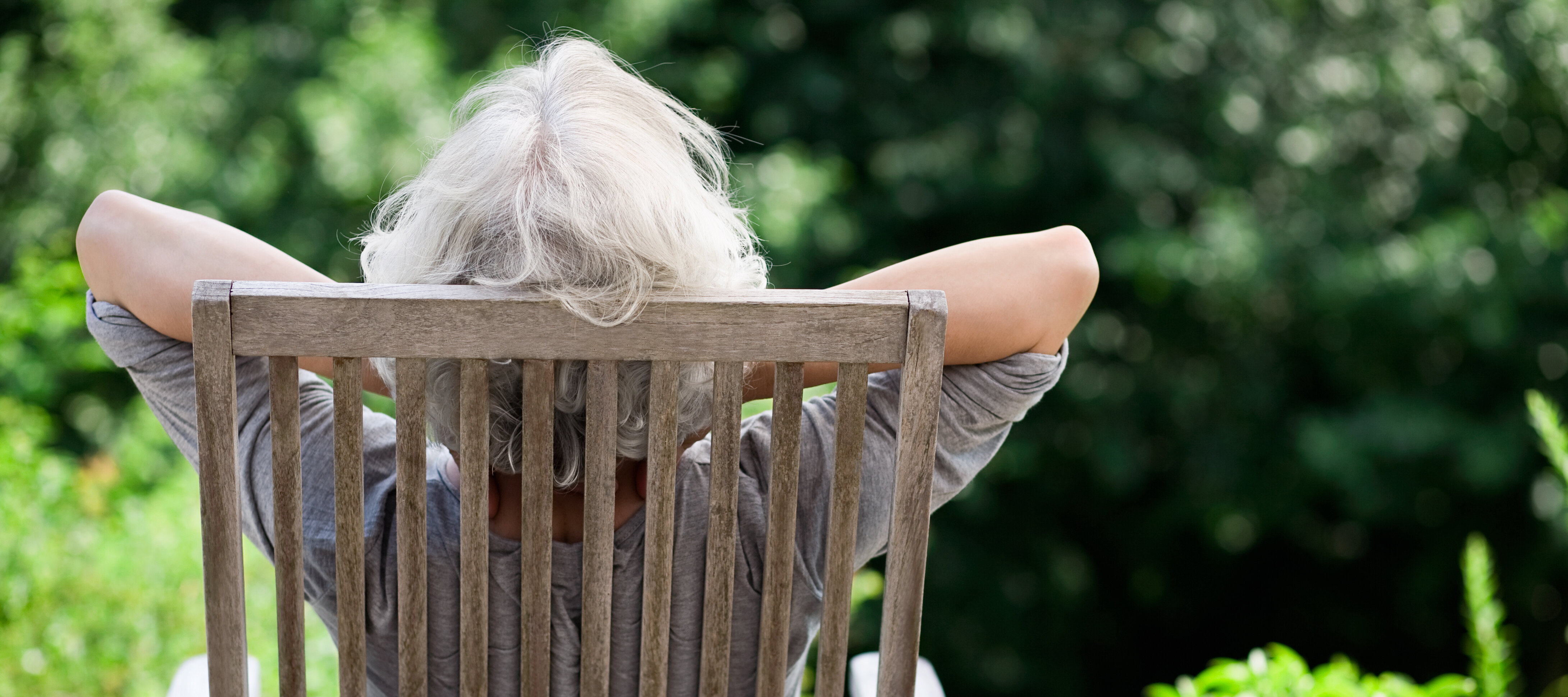 Rückenansicht einer älteren Frau, die auf einem Gartenstuhl im Grünen sitzt