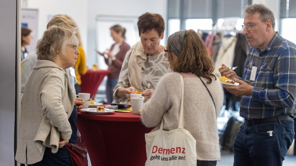 Kaffeepause im Foyer Foto: Vier Personen unterhalten sich und essen Kuchen am Stehtisch während der Pause.