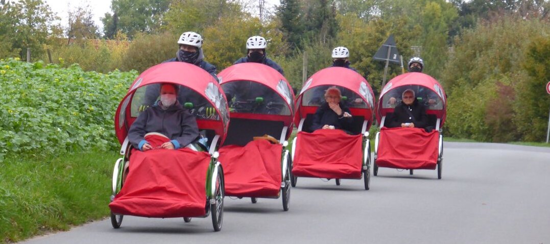 Foto: Personen, die in 4 roten Rikschas gefahren werden.