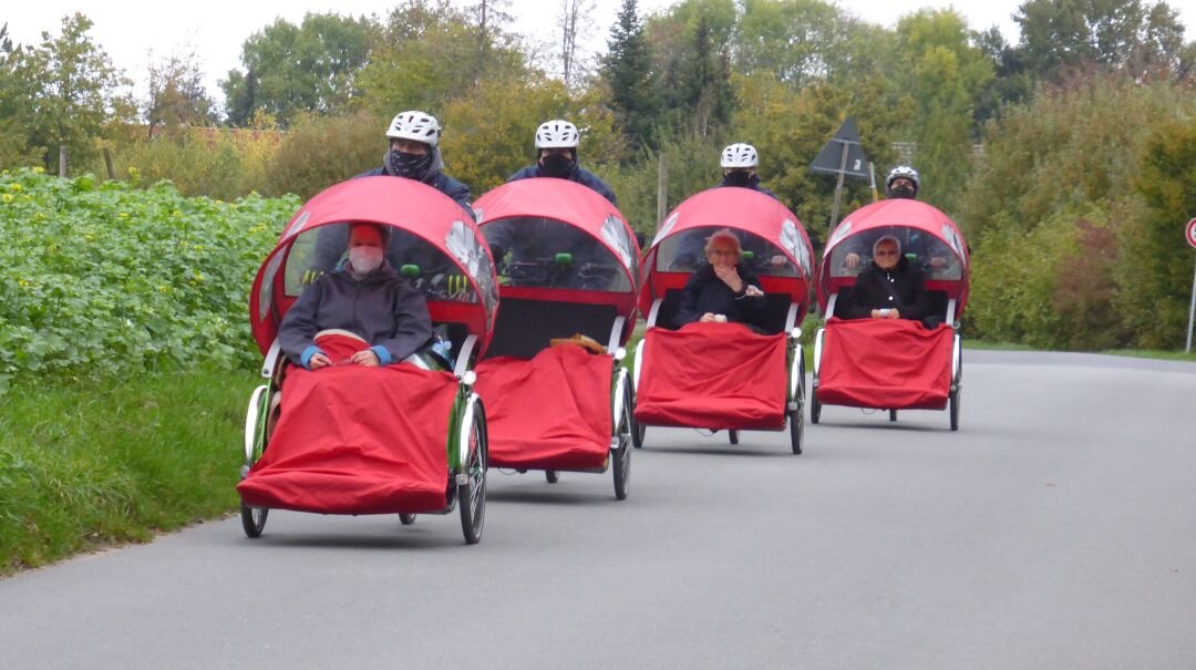 Foto: Personen, die in 4 roten Rikschas gefahren werden.