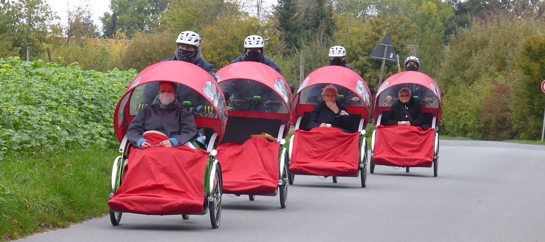 {Ausflüge mit der Rikscha machen – das geht auch unter Pandemie-Bedingungen Foto: Personen, die in 4 roten Rikschas gefahren werden.