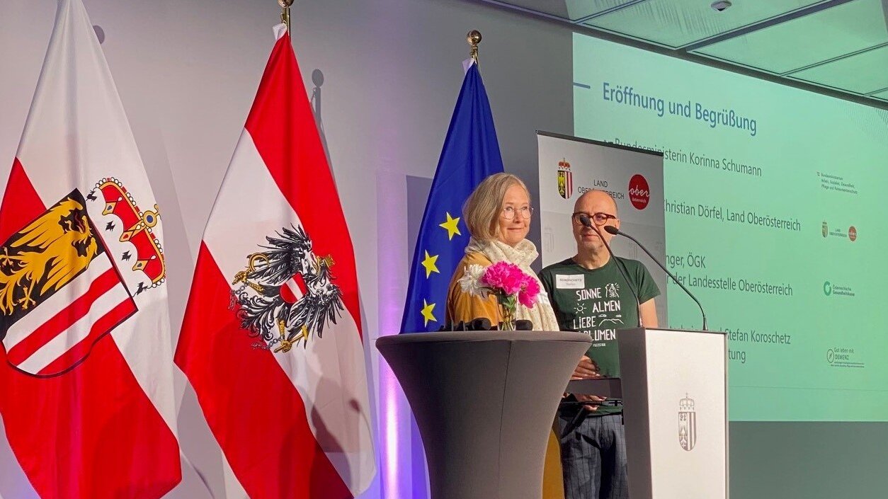 Angela Pototschnigg und Stefan Koroschetz stehen auf dem Podium und begrüßen die Teilnehmenden 