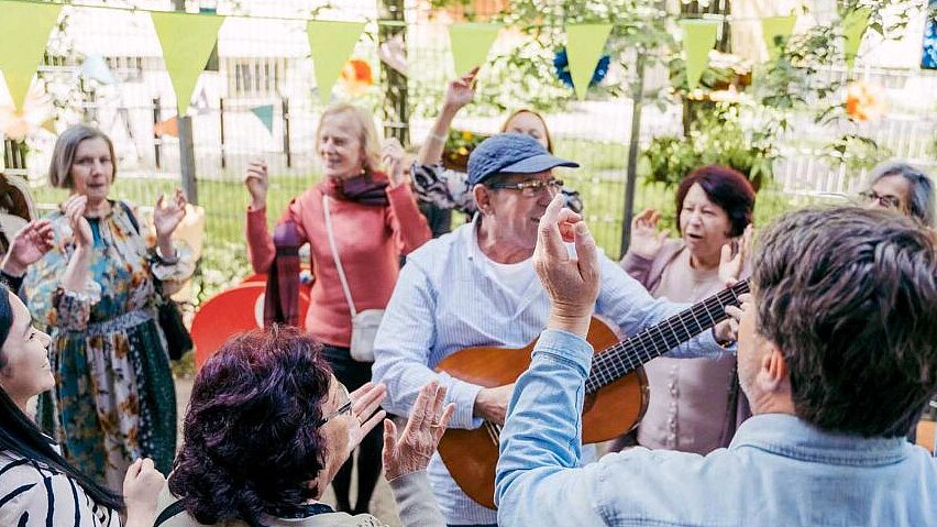 ©jennifer-kiowsky Feiernde Gruppe steht im Kreis mit einem Gitarristen in der Mitte