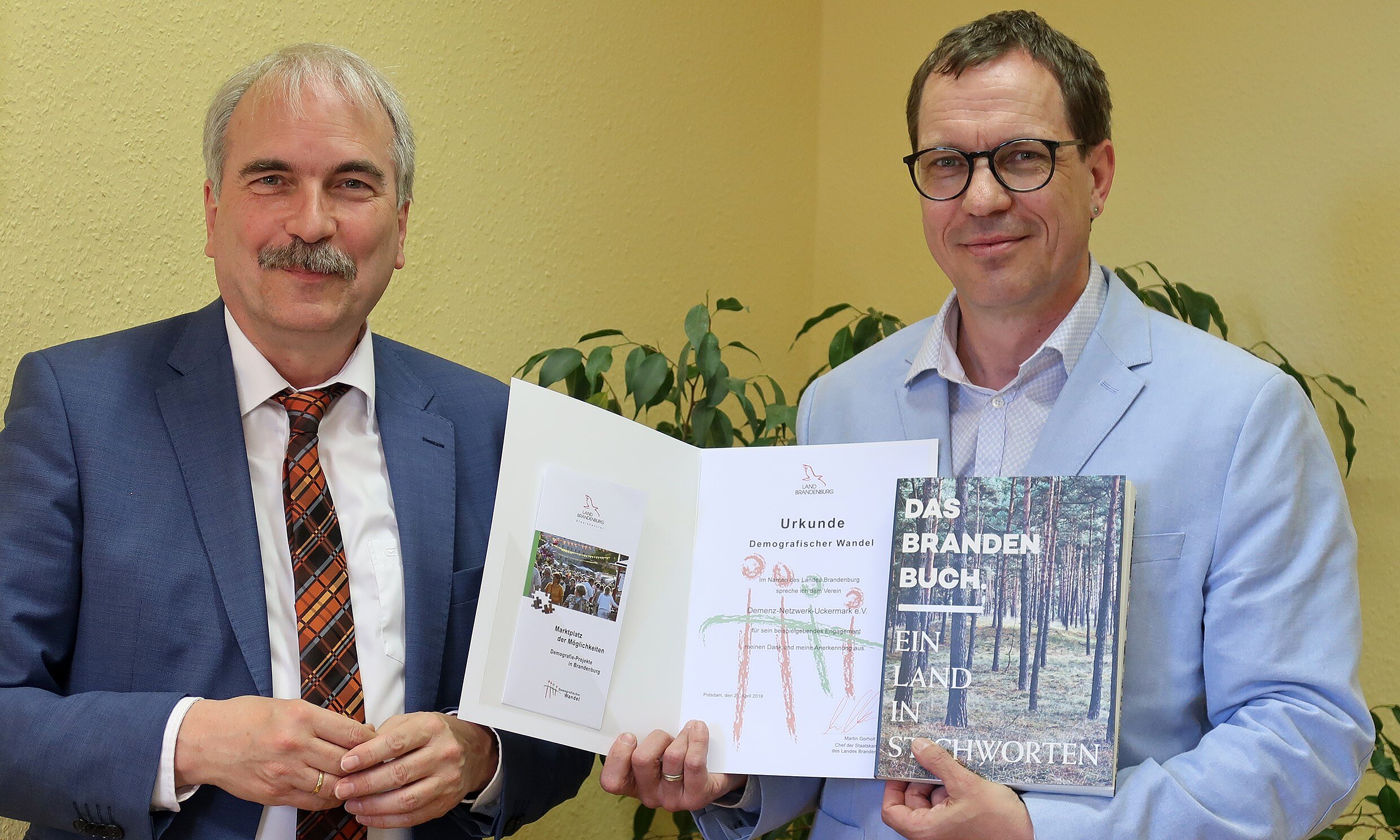 Foto: Zwei Herren werden fotografiert. Ein Mann hält eine Auszeichnung hoch.