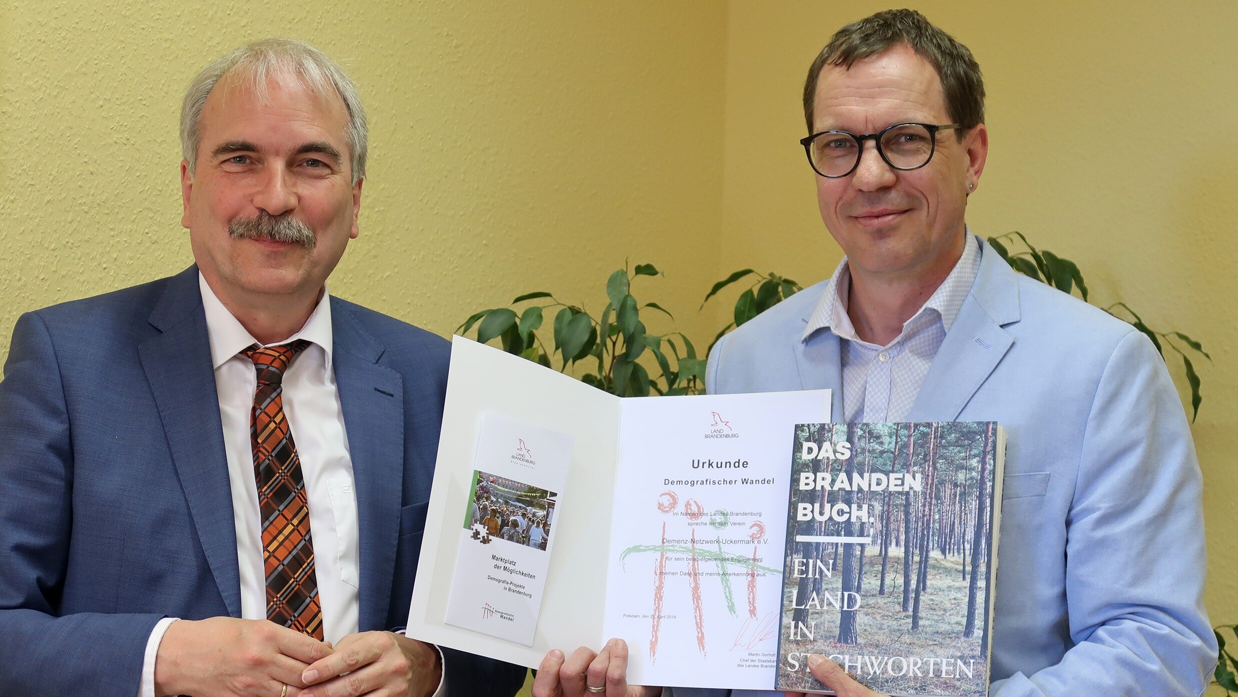 Foto: Zwei Herren werden fotografiert. Ein Mann hält eine Auszeichnung hoch.