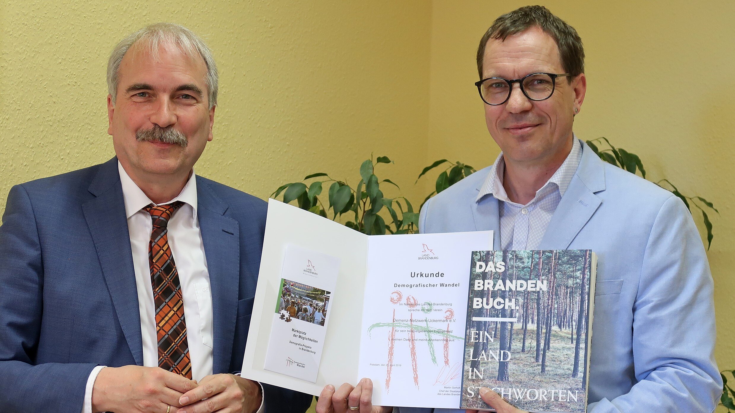 Foto: Zwei Herren werden fotografiert. Ein Mann hält eine Auszeichnung hoch.