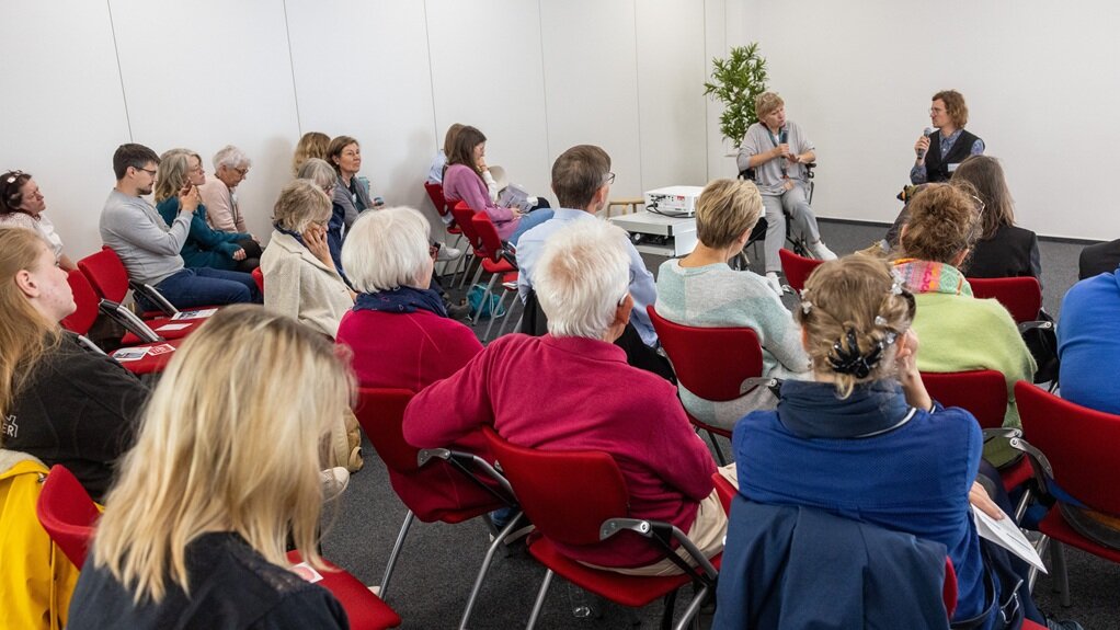 Im Dialog: Menschen mit und ohne Demenz sprechen über ihre Erwartungen und Wünsche Foto: Zwei Personen sitzen auf der Bühne und unterhalten sich. Das Publikum hört zu.