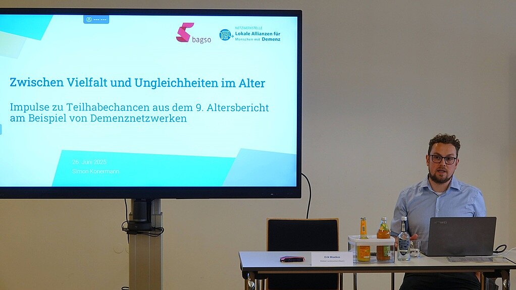 Simon Konermann am Laptop. Hinter ihm ist auf einem großen Bildschirm die Startseite seiner Powerpointpräsentation zu sehen. 