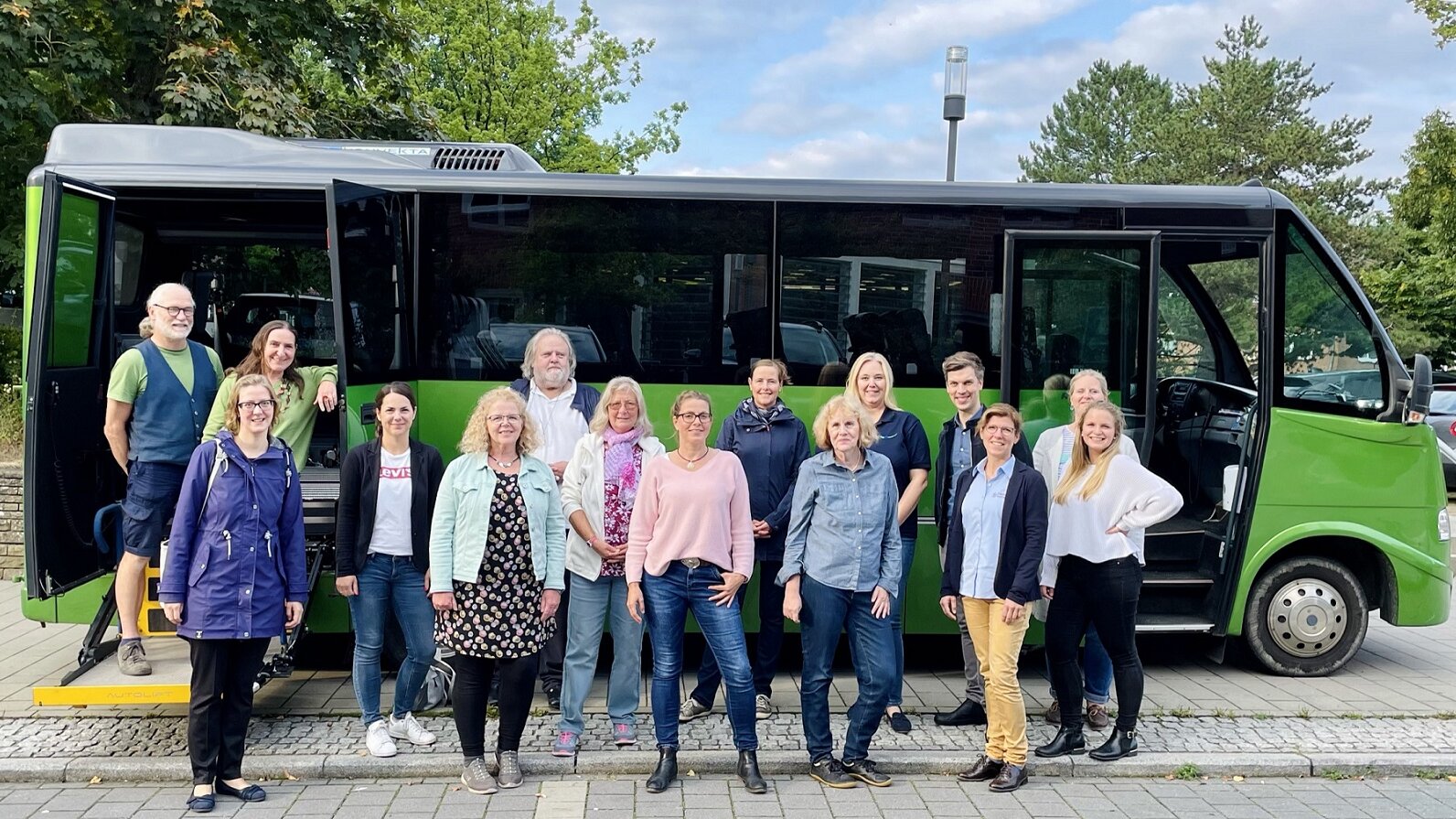 Foto: Gruppenfoto mit 15 Männern und Frauen aus der Lokalen Allianz vor dem grünen Bus