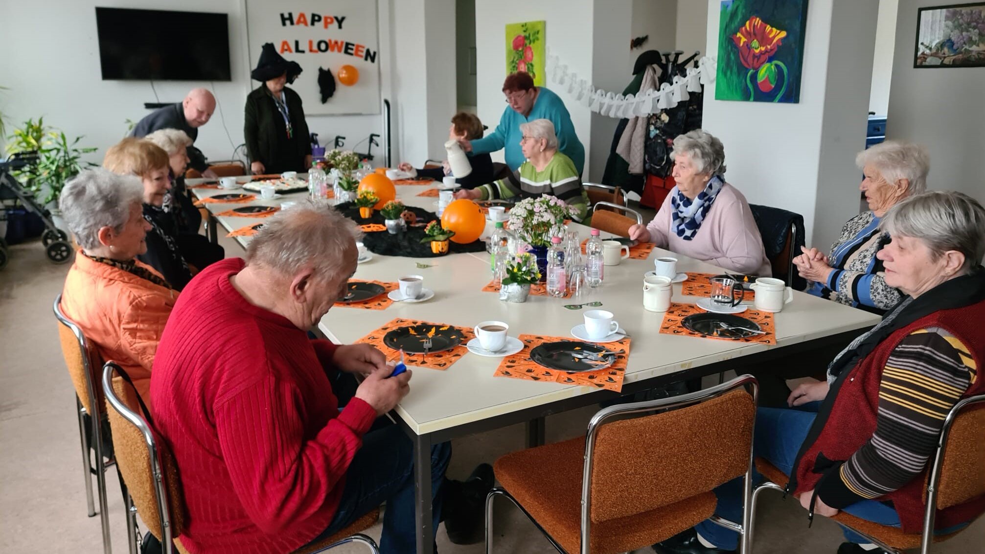 Foto: Eine Gruppe älterer Menschen sitzt an einem Tisch. Der Raum ist für Helloween dekoriert.  