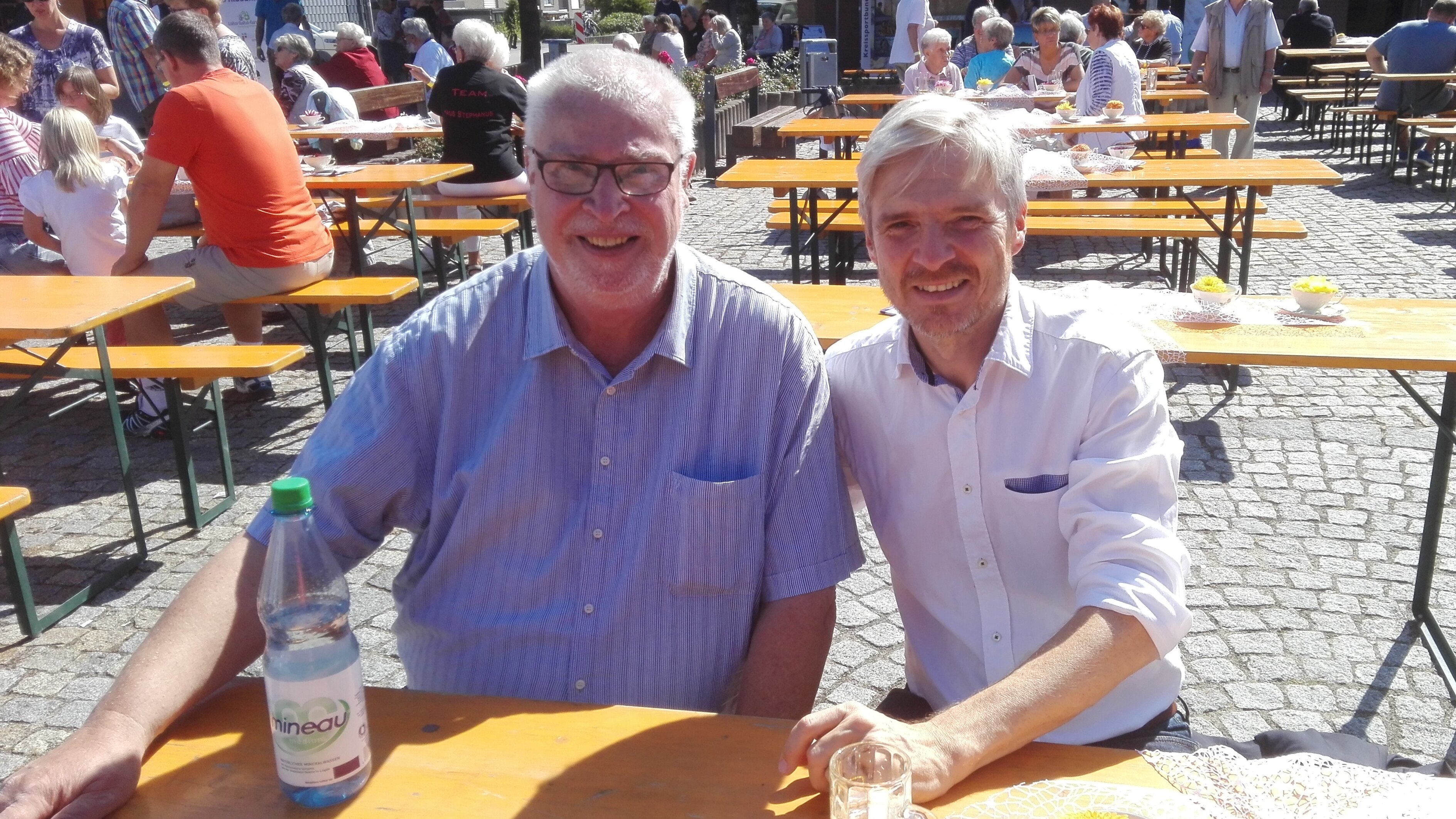 Auf diesem Foto sehen Sie zwei Männer, die an einem Biertisch sitzen. 