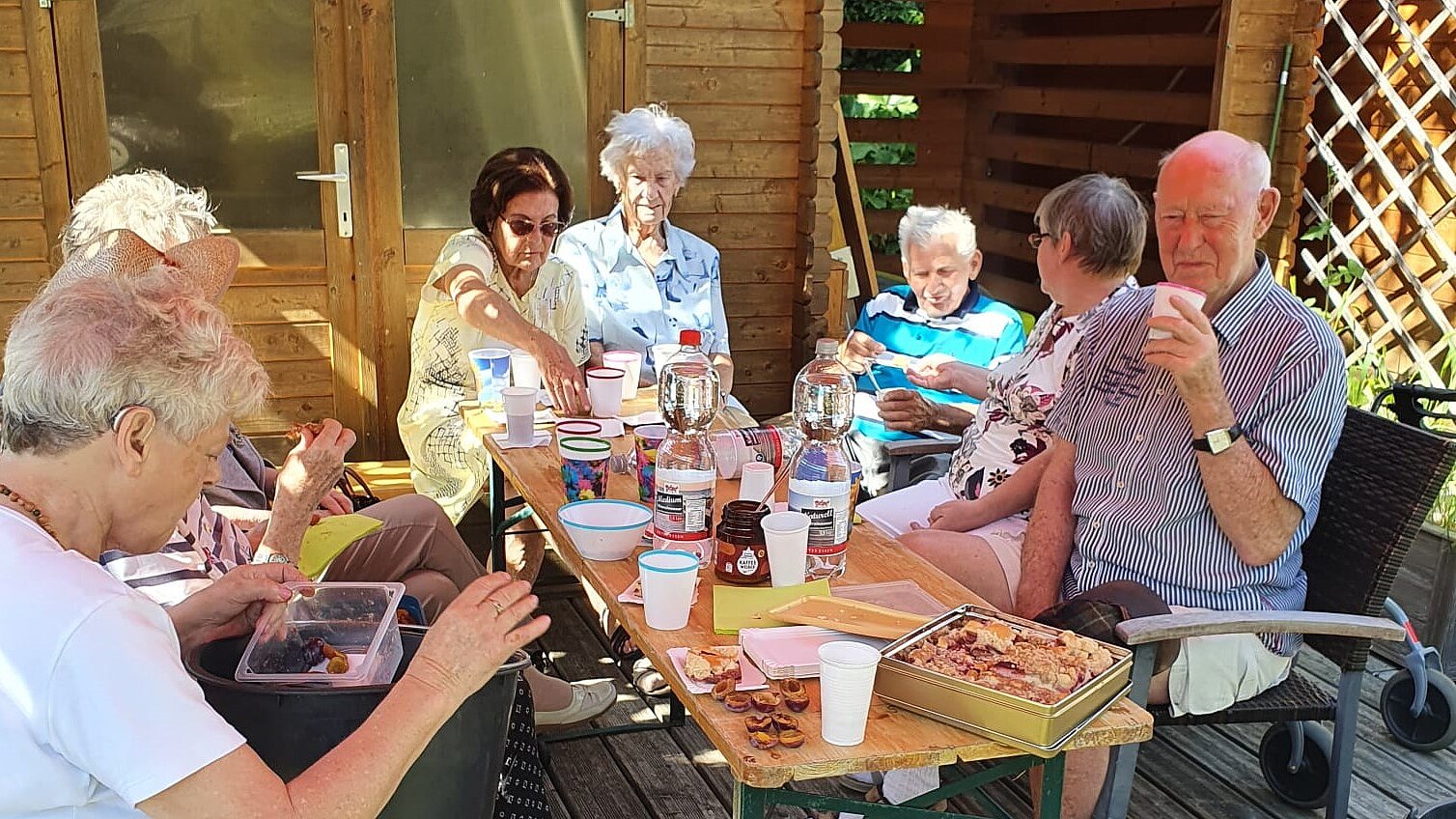 Die Rostocker Aktivgärtnerinnen und -gärtner in Aktion – und beim Kaffeetrinken Foto: Eine Seniorengruppe sitzt draußen beim Vespern um einen reichlich gedeckten Holztisch.