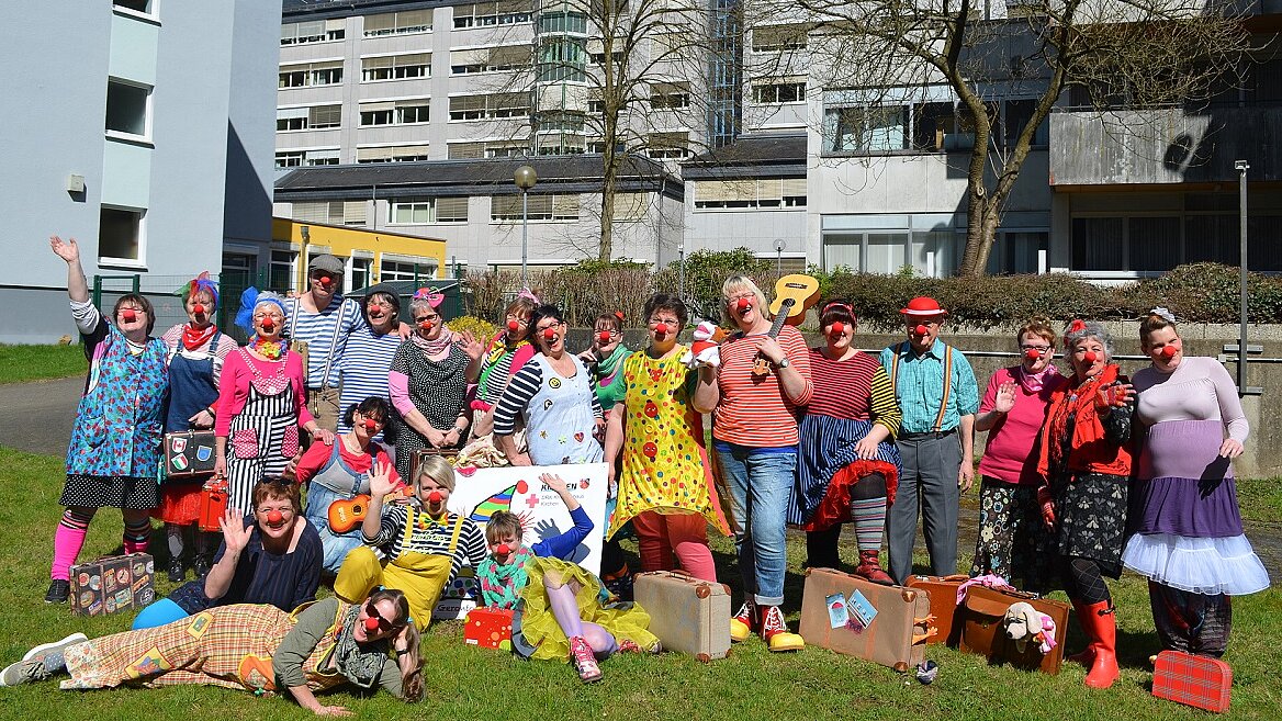 Gruppenbild von Frauen und Männern auf einer Wiese. Alle sind als Clowns verkleidet. 