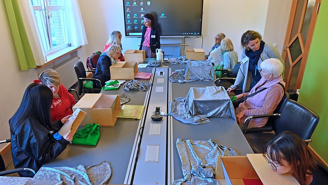 Demenz-Parcours „Hands on dementia“ zum Ausprobieren | „Demenz-Info-Tag“, Oktober 2024 in Stuhr Foto: 10 Personen sitzen an einem großen Konferenztisch, darauf Kartons mit Material zum Demenz-Parcours