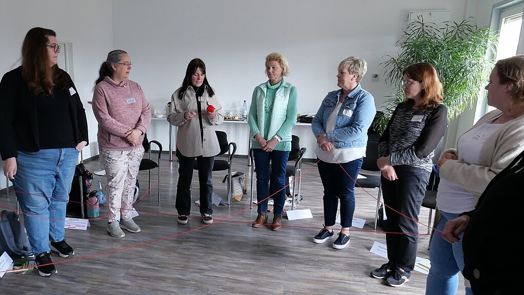 Die Teilnehmenden stehen im Kreis. Mithilfe eines roten Wollknäuels spinnen sie in ihrer Mitte ein Netz