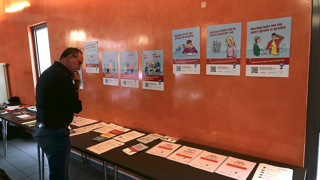 Ein Mann steht vor einem Tisch, auf dem Flyer und Broschüren liegen