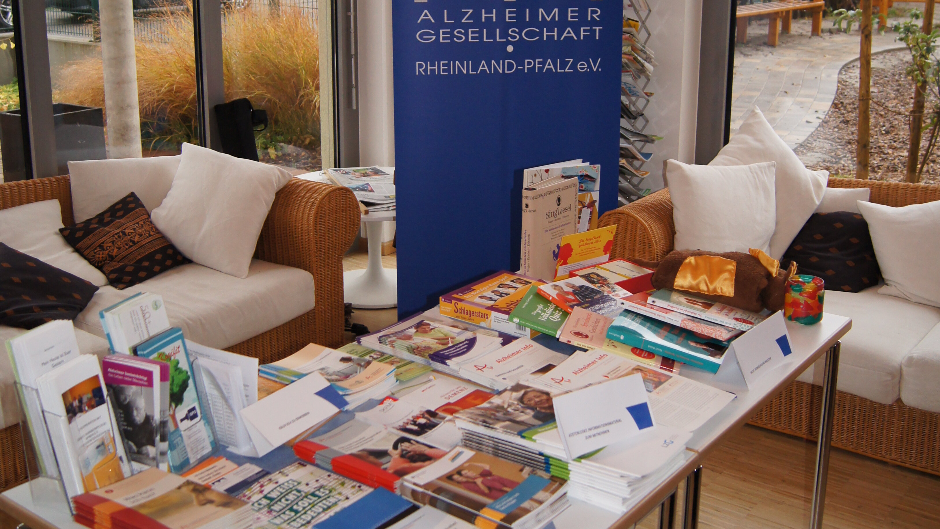 Foto: Ein Tisch, auf dem viele Informationsmaterialien der Alzheimergesellschaft liegen. Im Hintergrund steht ein Roll Up der Alzheimergesellschaft.
