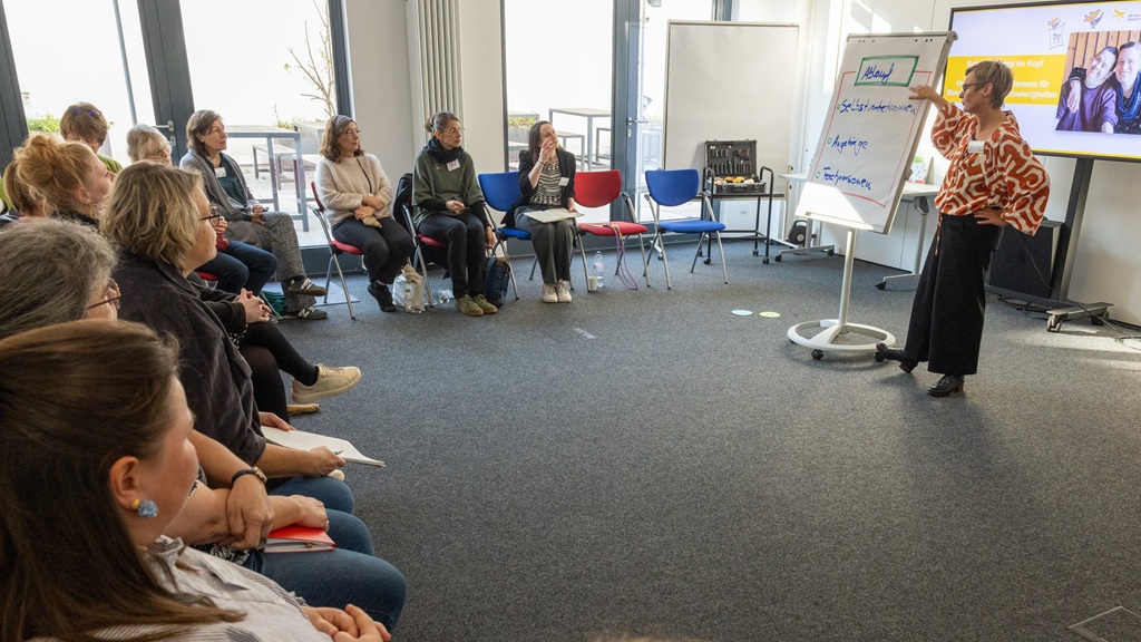 Referentin Dr. Anja Rutenkröger (Demenz Support Stuttgart) mit Teilnehmenden im Workshop "Demenz und Down-Syndrom – Schmetterlinge im Kopf" Foto: Refierende trägt im Workshop "Demenz und Down-Syndrom" etwas vor.