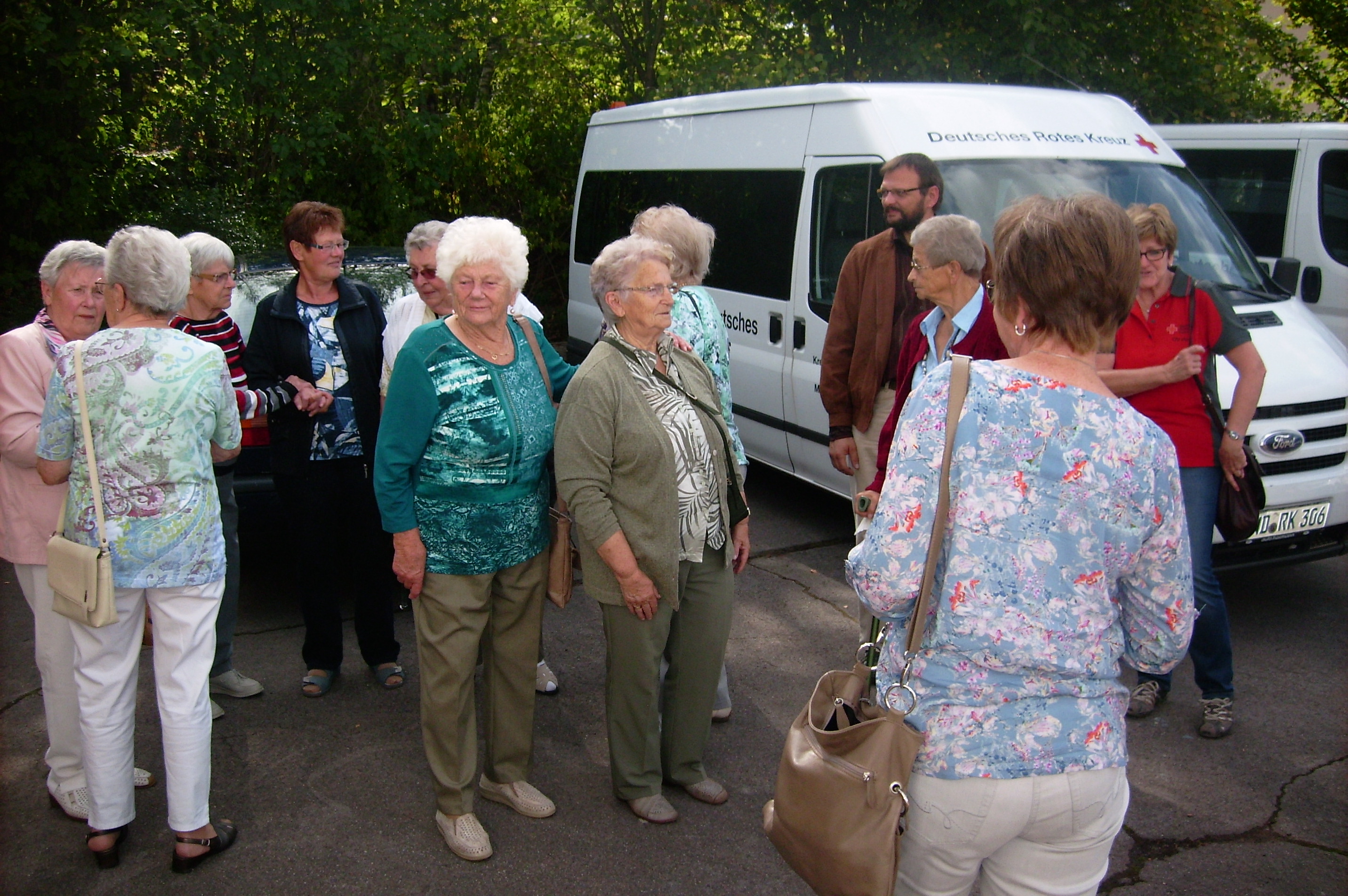 Eine Gruppe älterer Menschen steht mit der Dorfschwester Annetraud Kling auf einem Parkplatz