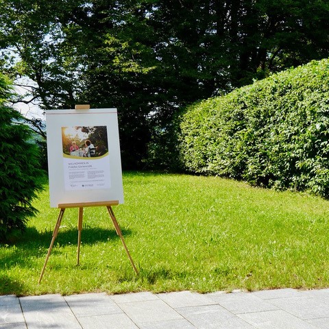 Im Garten steht eine Flipchart. Darauf ist ein Begrüßungsplakat für Friedas Gartencafé 